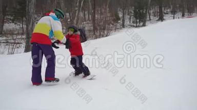 年轻人滑雪板教练教小男孩如何骑滑雪板。 冬季活动概念